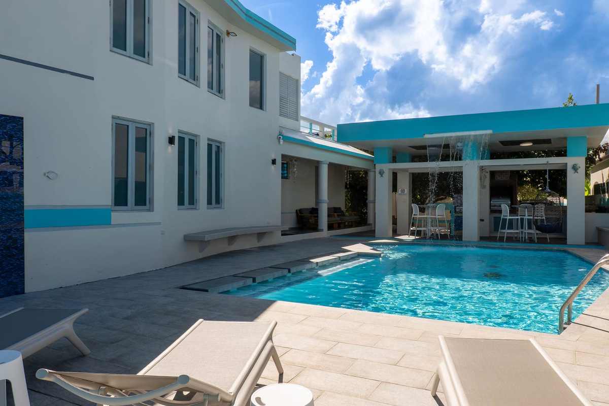White facade of the house rising over the pool terrace under a blue sky
